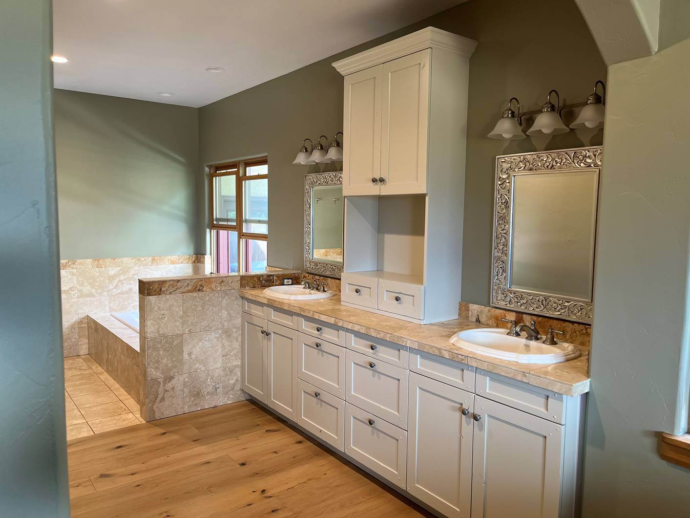 The same master bathroom after cabinet painting, with white vanity cabinets and soft sage walls