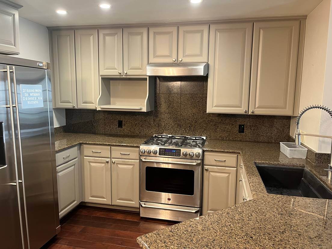Kitchen after cabinet refinishing, with dated wood cabinets painted a warm cream and finished with a smooth sprayed surface