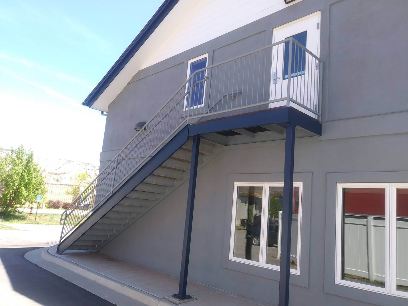Two story exterior after painting in Collier County, with grey stucco, navy steel stairs and white railings against a clear sky