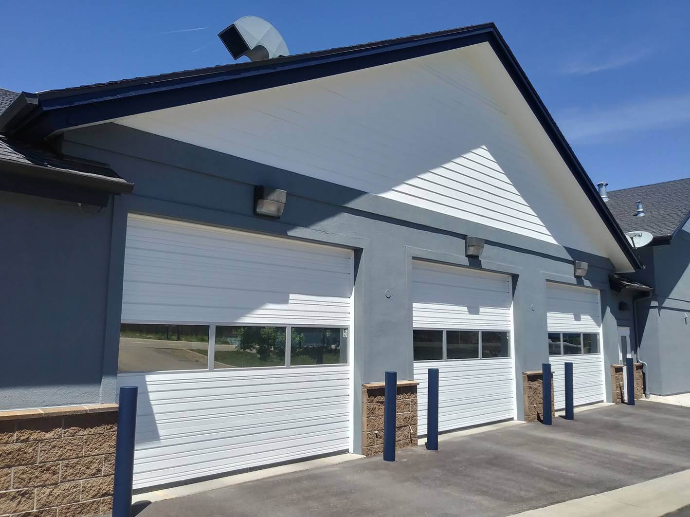 Commercial building after exterior painting, with charcoal stucco, white overhead bay doors and navy trim