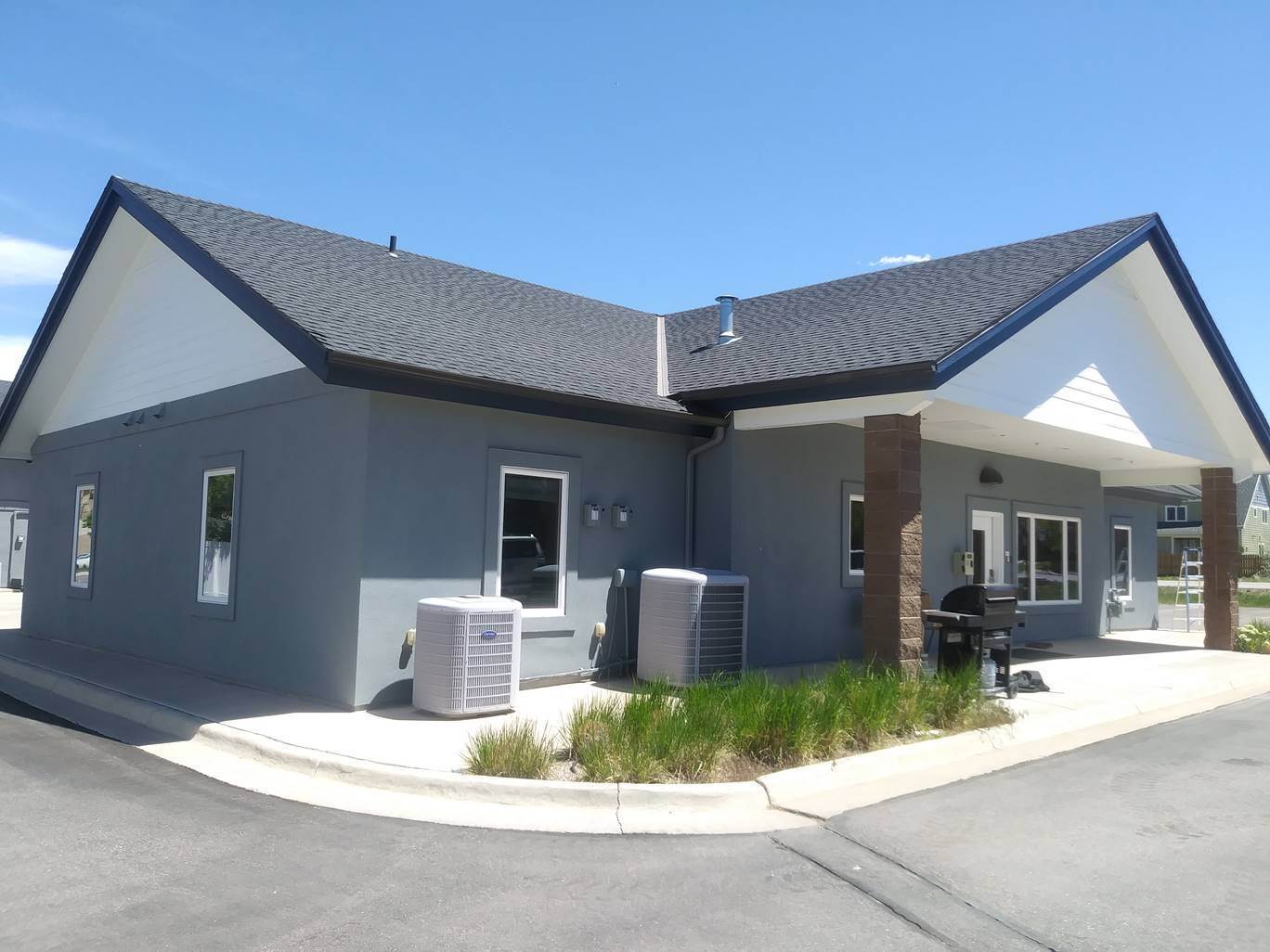 Commercial building exterior after a full repaint in charcoal grey with white gable siding and navy trim under a clear sky