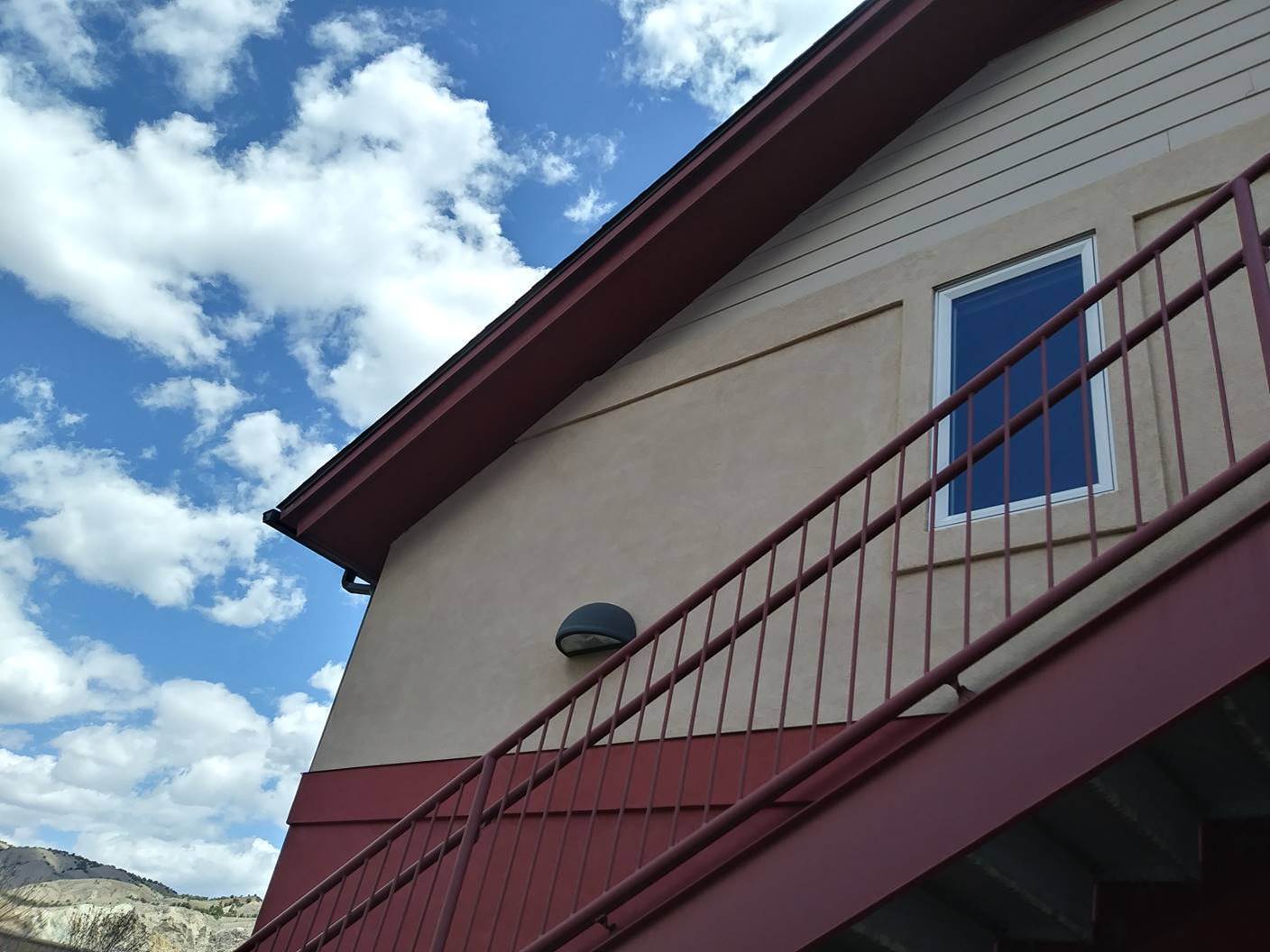 Freshly painted stucco exterior with deep red trim and repainted steel railing against a blue sky