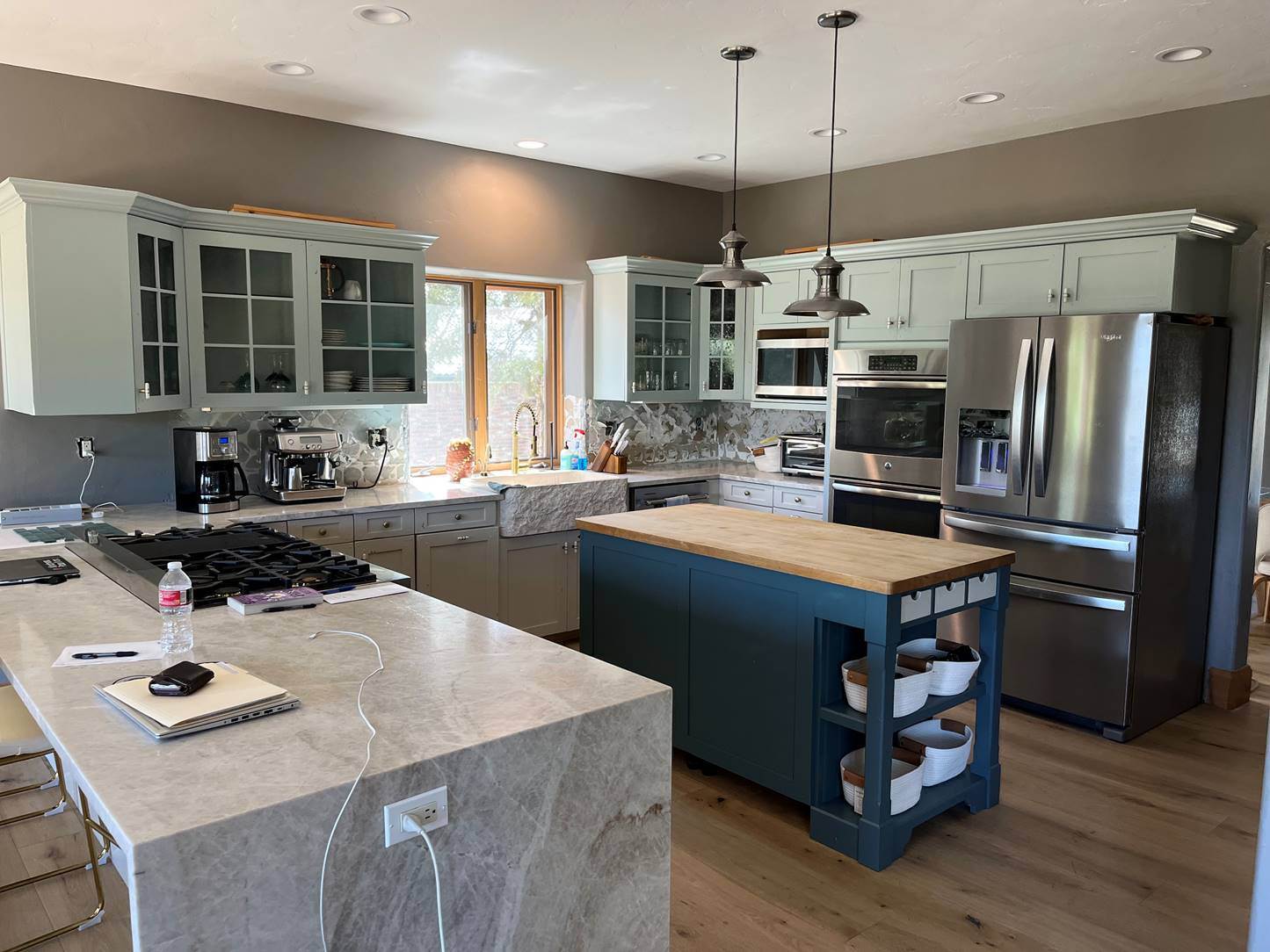 The same kitchen after cabinet painting, with soft sage green cabinets, a deep navy island and repainted walls