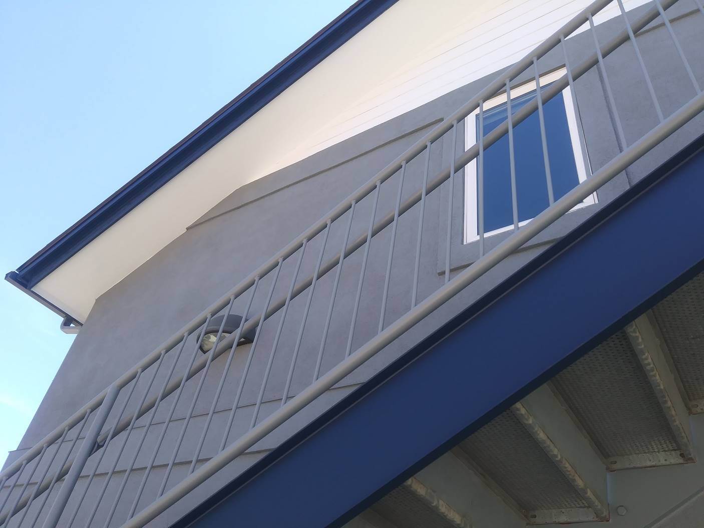 Repainted grey stucco exterior with navy fascia and white railings, a commercial exterior painting project by Sun Up Painting